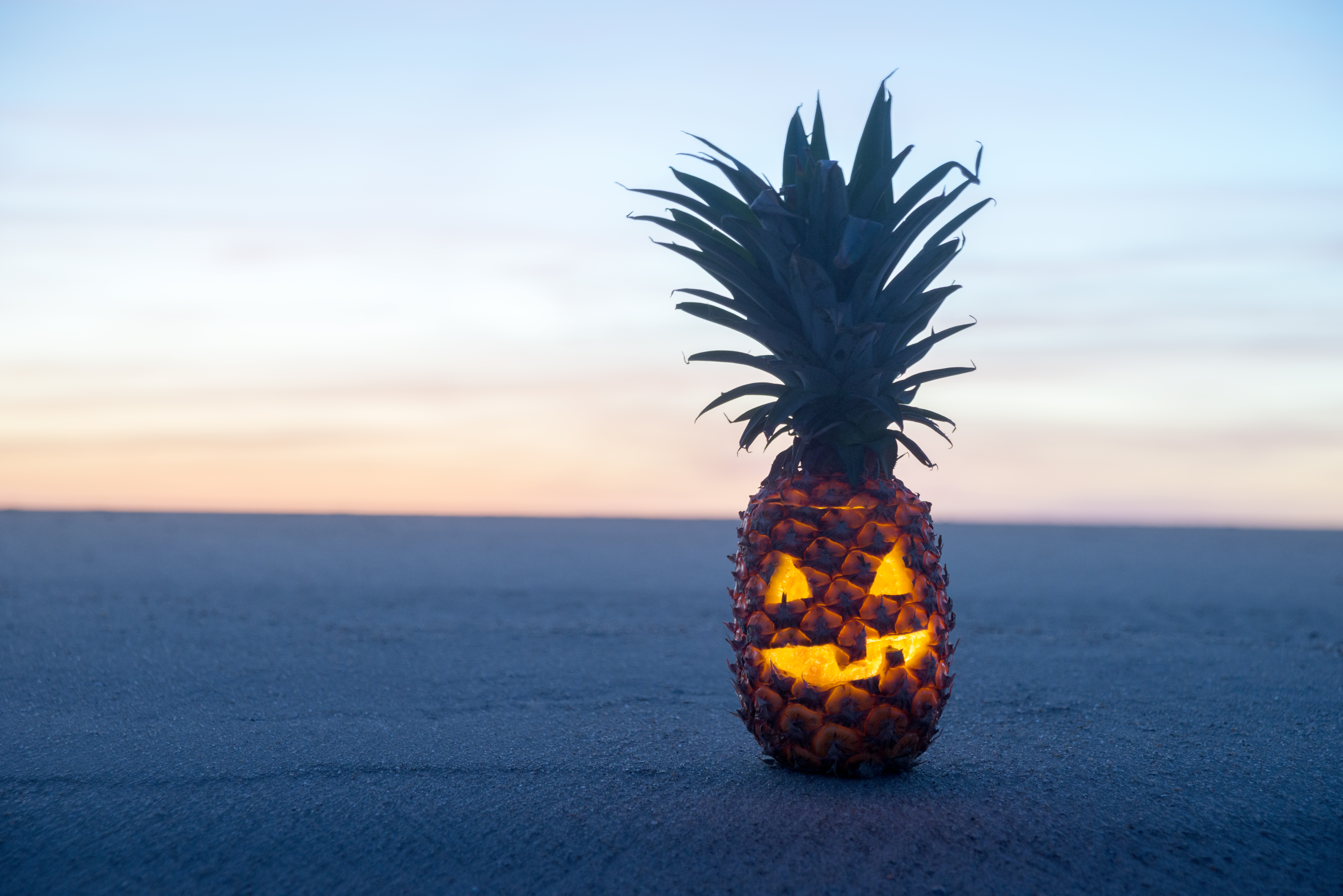 Pineapple carved like jack-o-lantern on the beach at sunset
